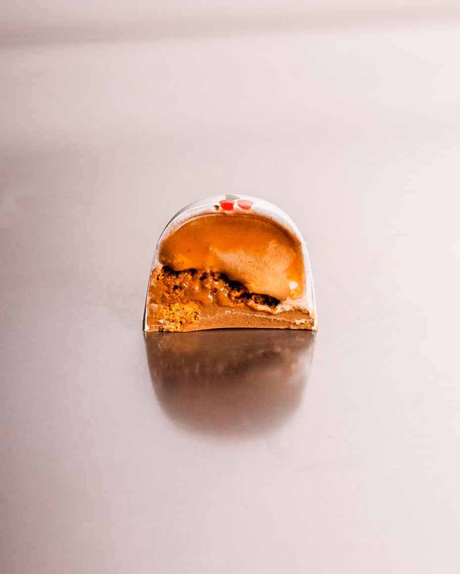 A domed chocolate cut open on a caramel and biscuit filling