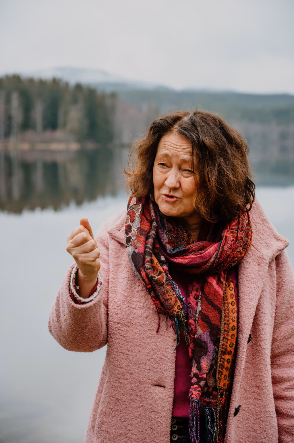 Angela Halvorsen Bogo telling a story beside a lake in a pink coat and scarf