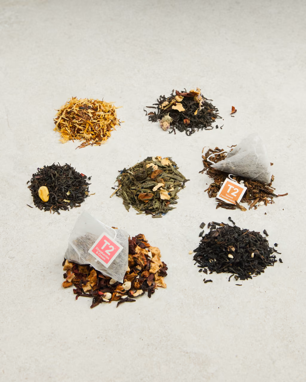Seven piles of loose tea leaves with three tea bags among them