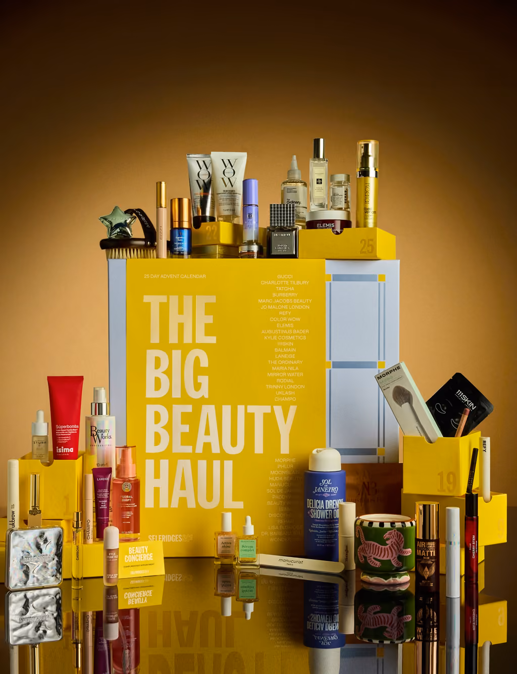 The Selfridges 2026 calendar lit warm, products arranged on the box and in front of it on a mirrored surface