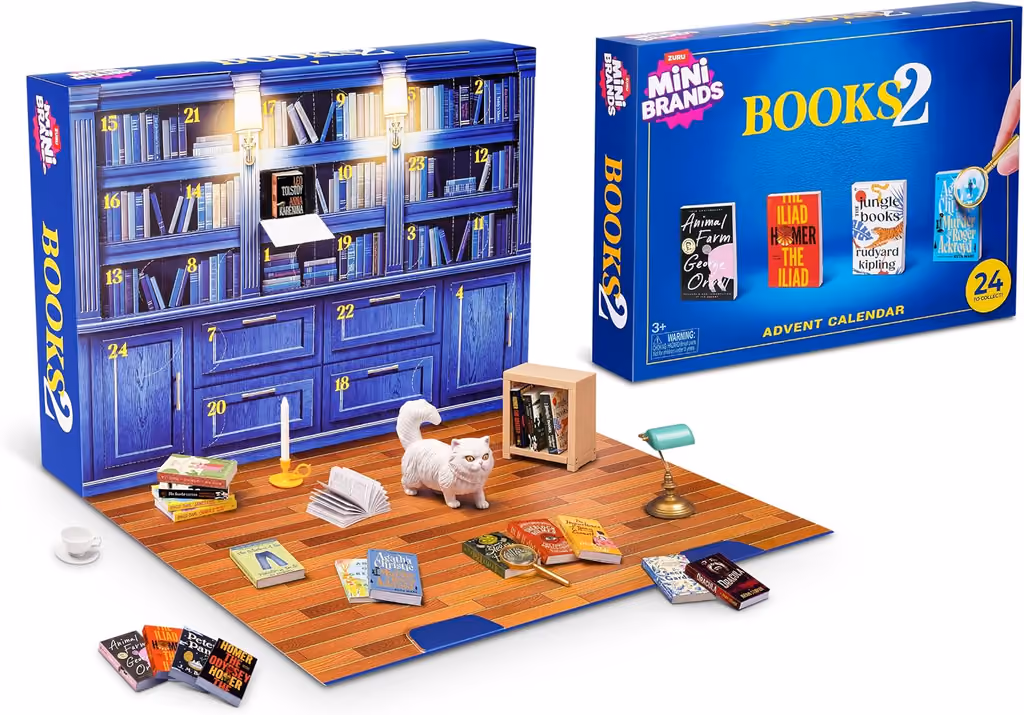 The bookcase box folded open onto its wooden-floor mat, mini books, a lamp, a shelf and a white cat in front