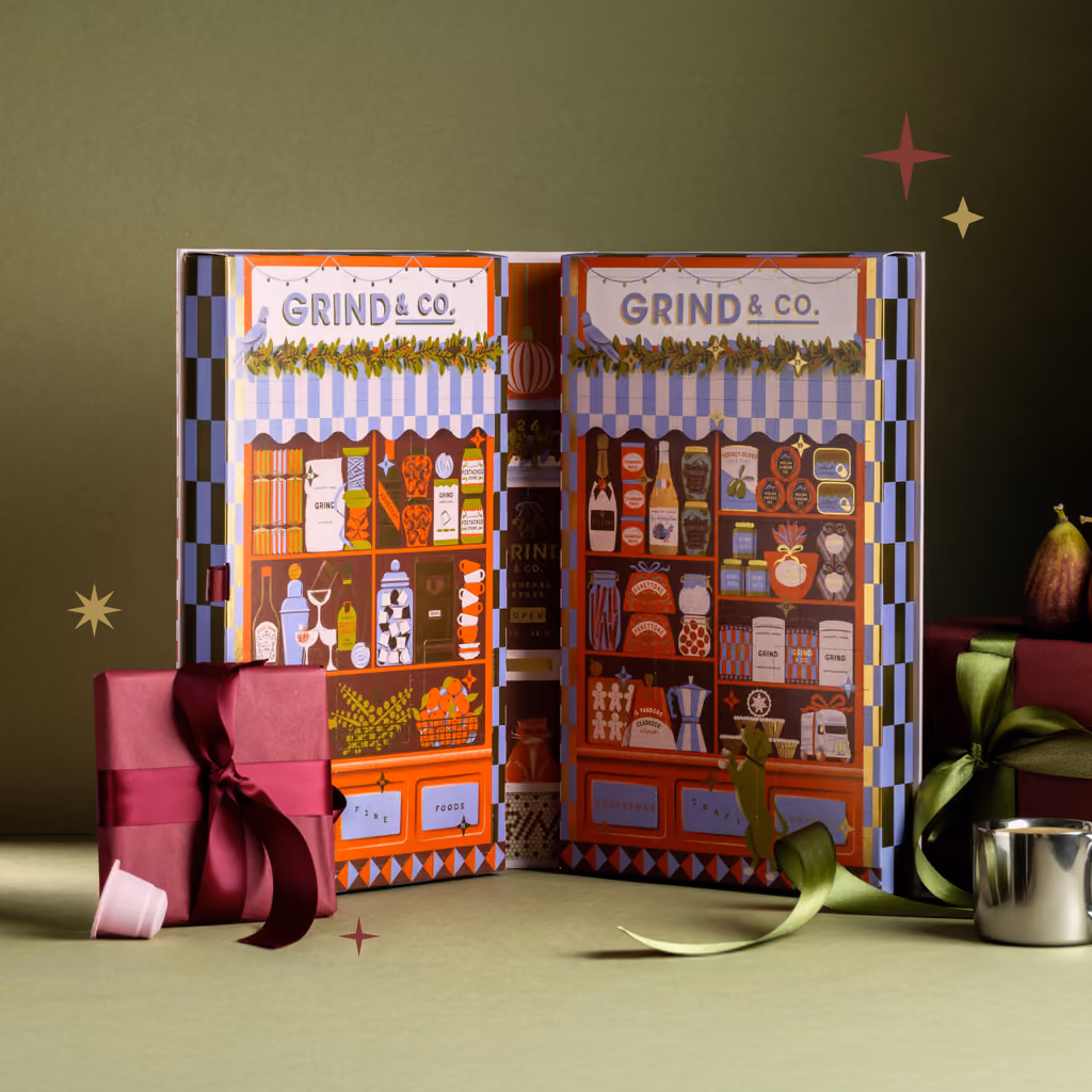 The open box on a table with a wrapped present and a cup beside it