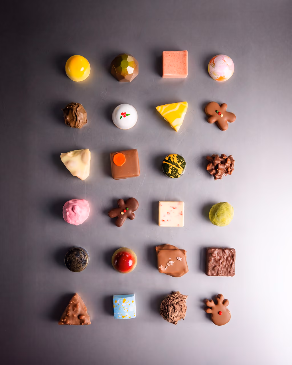 All 24 chocolates laid out in a grid on a grey ground