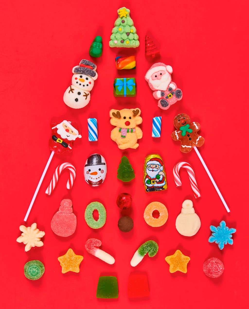 Christmas-shaped gummies and candy canes laid out in a tree shape on red