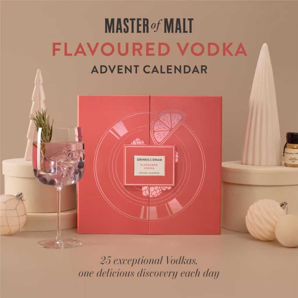 The pink box printed with citrus and berries on a beige set beside a cocktail